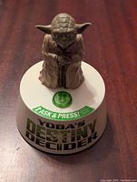 Front view of Yoda figure on the round white base with visible green button and text