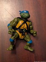 Front view of Leonardo action figure featuring green body, yellow chest, blue mask and guards, detailed face and hands.