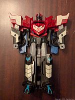 Front view of Optimus Prime figure in robot mode showing red chest with Autobot emblem, black and grey legs with blue highlights, and red and white arm panels.