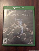 Front cover of the Xbox One game Middle-earth Shadow of War showing artwork of a warrior fighting orcs.