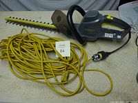 Full view of Yardworks electric hedge trimmer and the yellow extension cord coiled beside it