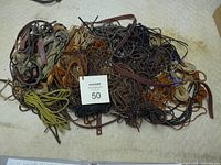 Top-down view of a large pile of mixed leather lacing in multiple colors and sizes spread out on a surface with a lot number card visible.