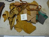 Photo of assorted leather scraps and leather lacing pieces in multiple colors and textures lying on a surface with a lot number card visible