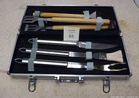 Complete BBQ tool set with six pieces displayed inside an open metal case showing wooden and stainless steel handles.