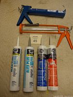 Full view of two caulking guns and four tubes of caulk placed horizontally on a beige surface.
