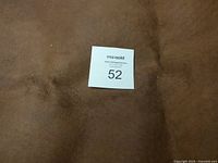 Close-up photo showing texture and color of the brown leather piece with the lot number tag.