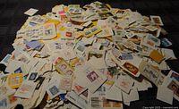 A large pile of used postage stamps from Canada and some other countries, attached to bits of envelopes and papers spread out on a surface.
