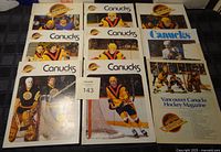 Top view of nine vintage Vancouver Canucks hockey programs with various players in black and yellow uniforms on cover, some showing visible wear and damage.