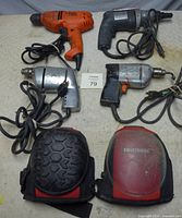 Overview of four corded drills and two knee pads laid out on surface