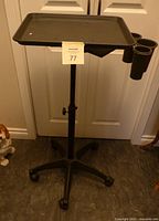 Front angled view of the black adjustable rolling tray with utensil cups, showing tray surface and height adjustment knob.