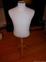 Full view of the white fabric shirt form torso on wooden tripod stand against a wood floor background.