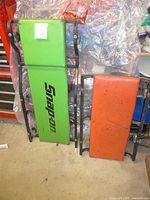 Green Snap-on padded mechanics creeper and orange padded short creeper leaning against a wall, showing overall condition and size difference.