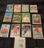 Twelve 1970s NHL hockey cards laid out on dark cloth including players Dryden, Esposito, Bossy and others with a trademark sticker patch on the side.