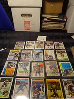 Photo shows 20 hockey cards laid out on a black grid surface, displaying various players and teams from the 1980s NHL. Cards are in protective sleeves and arranged in 4 rows.