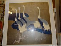 Framed crane print showing five cranes with mostly brown textured background and blue river. Silver frame visible at edges.