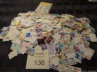 Pile of assorted postage stamps spread out on a dark surface showing a large quantity with varied designs and colors.