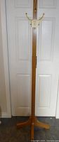 Full view of the wooden coat tree against a white door showing overall height and leg spread.