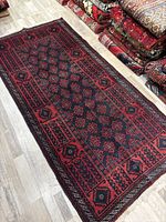 Full view of Baluchi rug laid flat among other rugs