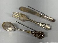 Top angle view of the three silver cutlery brooches arranged side by side showing front details.