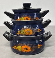 Stacked view of the three blue enamel casserole pots with floral orange and yellow patterns and black handles.