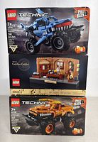 Three boxed LEGO sets stacked showing front of each box: Monster Jam Megalodon, Galileo Galilei tribute, and Monster Jam Max-D.
