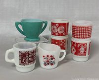 Photo showing six vintage cups including five Fire King mugs with red and white patterns and one turquoise handled cup.