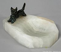 Front-right angled view showing white marble dish with beveled edges and attached bronze Scotty dog figurine standing at edge.