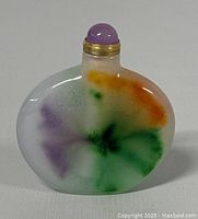 Front view of the small rounded flat jadeite bottle showing multicolored hues and purple stopper with gold collar.