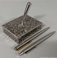 Close side-angle view of the vintage covered pen holder with two Parker pens beside it.