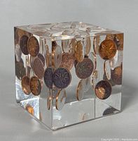 Clear Lucite acrylic cube paperweight featuring embedded Canadian pennies suspended within, showing various penny faces and edges, polished finish visible.