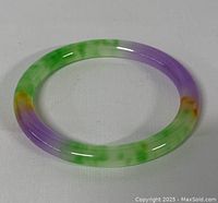Front view of round jade bangle showing green, purple, and amber colors against white background