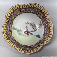 Top view of a lotus-shaped hand-painted ceramic bowl showing an Asian woman beneath a blossoming tree in the center, surrounded by a detailed yellow and pink floral border.