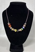 Front view of the necklace on black display bust, showing the arrangement of glass and metal beads on the dark brown cord.
