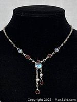 Front view of sterling silver chain necklace with multiple moonstone and garnet stones and central pendant with dangling garnet drops, displayed on black bust.