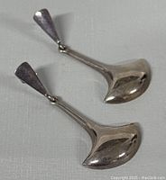 Pair of polished sterling silver drop earrings with broad teardrop-shaped stud and elongated rounded spoon-shaped drop pendants lying flat on gray surface.