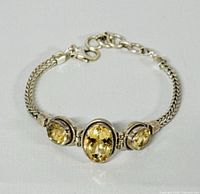 Close-up of bracelet showing three oval faceted citrine gemstones set in sterling silver and woven silver chain.