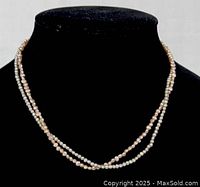 Front view of the double strand pearl necklace displayed on black stand showing two strands of small pearls in pink and ivory tones.