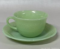Green jadeite glass teacup on matching saucer shown upright, highlighting shape and pattern.