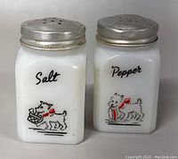 Front view of both milk glass salt and pepper shakers with Westie dog illustrations and metal tops.