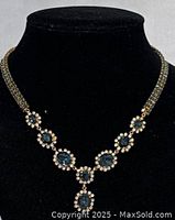 Front close-up of vintage rivière necklace showing blue stones surrounded by clear stones in gold-tone setting.