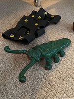Photo showing the green cast iron boot jack and one black winter boot tread with yellow cleats lying on carpet.