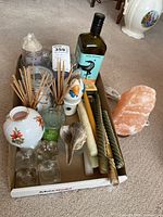 Salt lamp on wood base with power cord next to olive oil bottle, candles, reed diffusers, glass candle holders, and ceramic duck candle holder all arranged on floor inside a box