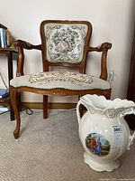 Front view of carved wooden armchair with detailed cross stitch upholstery showing floral and classical themes.