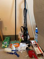 Photo of Eureka upright vacuum cleaner with manuals, various cleaning supplies, dusters, and a small red hand vacuum in the foreground.