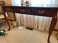 Front view of mahogany wooden console table showing the center drawer and two false drawers, with curved Queen Anne legs and brass handles.