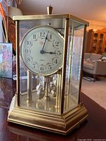 Front angled view of the Elgin anniversary clock showing the round white face, brass frame, and rotating pendulum balls inside.