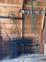 Mixed garden fencing, trellises, and shepherd's hooks arranged in shed with wooden walls.