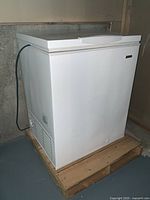 Full side angle view of white Kenmore chest freezer placed on wooden platform in basement.