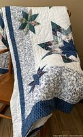 Quilt draped over wooden chair showing border and star patterns on white background.
