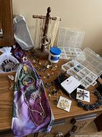 Full lot display showing jewelry stand with pearl necklaces, bracelets, container of cleaning cream, colorful scarf, two brooches on cards, assorted costume jewelry items in organizer boxes and laid on table.